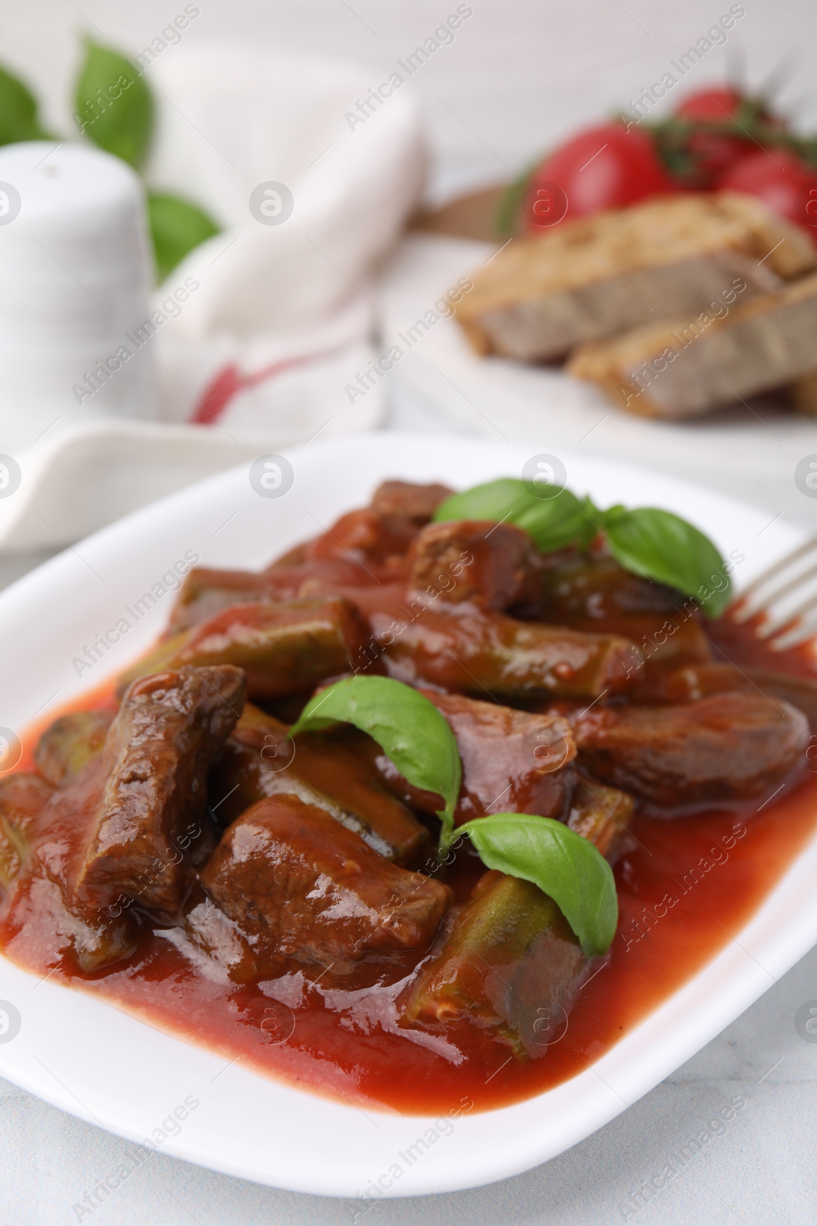 Photo of Tasty stew with okra, tomato sauce, bread and basil on white tiled table, closeup