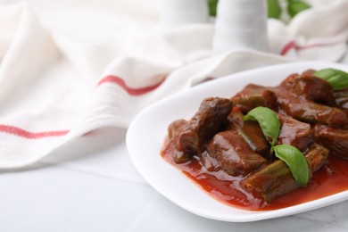 Tasty stew with okra, tomato sauce and basil on white tiled table, closeup. Space for text