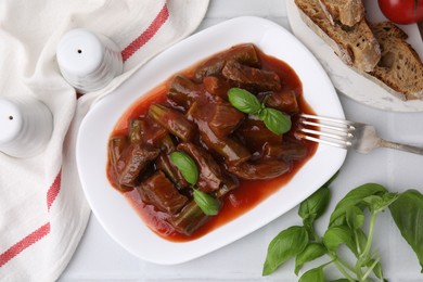 Photo of Tasty stew with okra, tomato sauce, bread and basil on white tiled table, flat lay