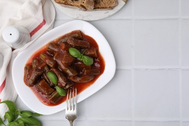 Tasty stew with okra, tomato sauce, bread and basil on white tiled table, flat lay. Space for text