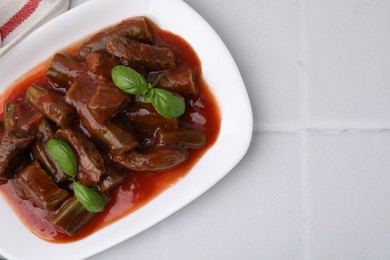 Tasty stew with okra, tomato sauce and basil on white tiled table, top view. Space for text