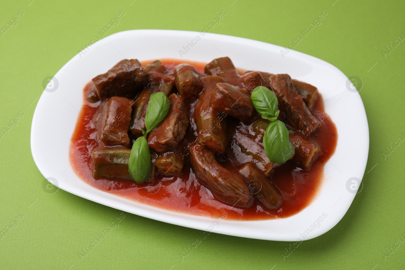 Photo of Tasty stew with okra, tomato sauce and basil on light green background, closeup