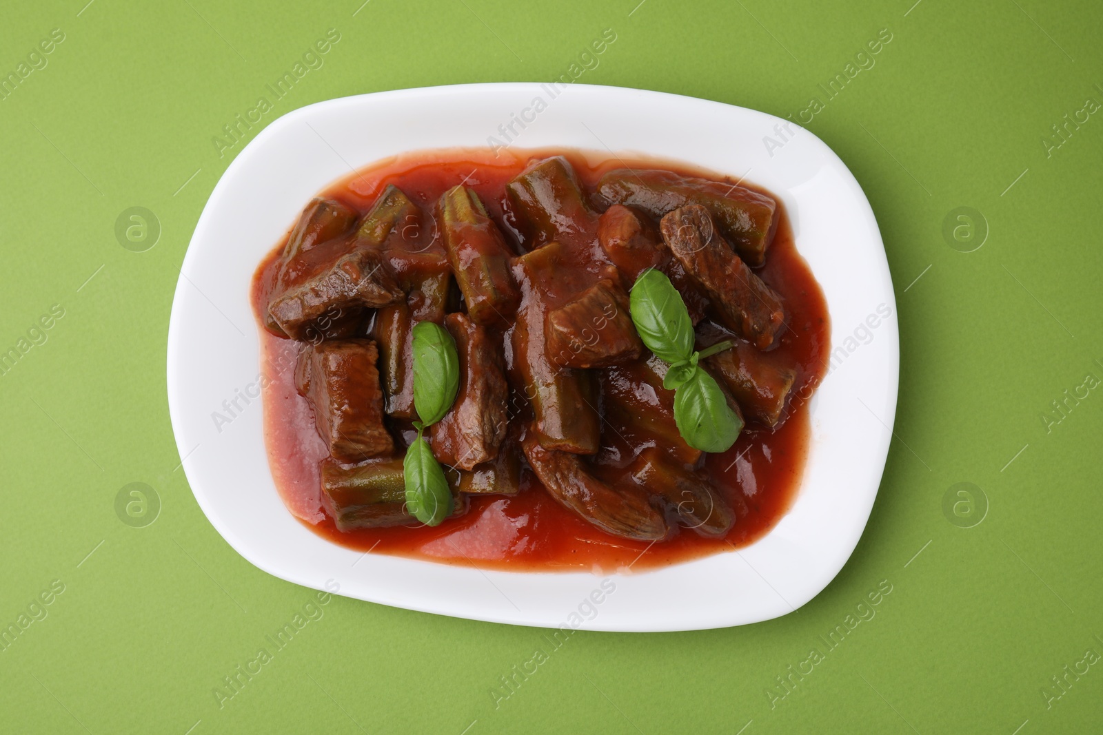 Photo of Tasty stew with okra, tomato sauce and basil on light green background, top view