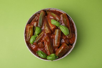 Tasty stew with okra, tomato sauce and basil on light green background, top view