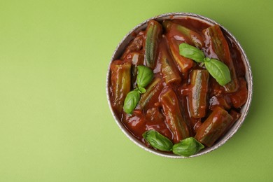 Tasty stew with okra, tomato sauce and basil on light green background, top view. Space for text