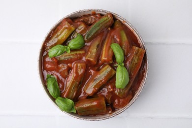 Photo of Tasty stew with okra, tomato sauce and basil on white tiled table, top view