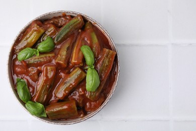 Tasty stew with okra, tomato sauce and basil on white tiled table, top view. Space for text