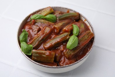 Photo of Tasty stew with okra, tomato sauce and basil on white tiled table, closeup