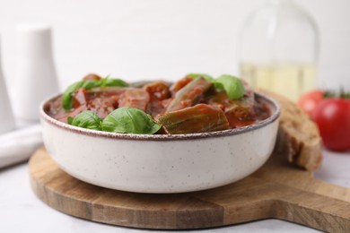 Tasty stew with okra, tomato sauce and basil on white tiled table, closeup