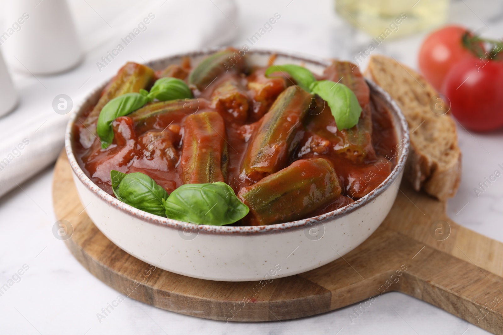 Photo of Tasty stew with okra, tomato sauce and basil on white tiled table, closeup