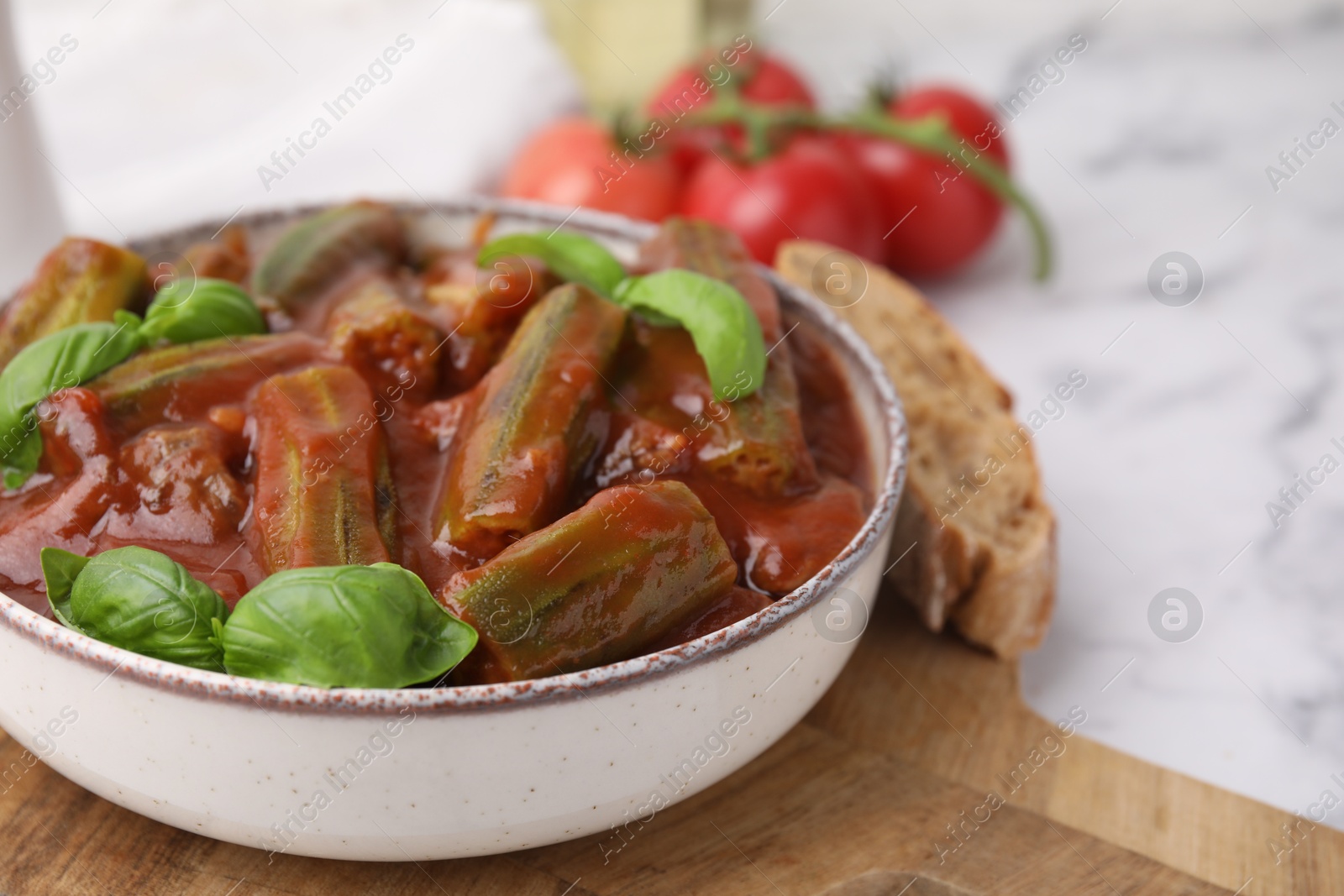 Photo of Tasty stew with okra, tomato sauce and basil on white marble table, closeup