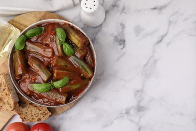 Photo of Tasty stew with okra, tomato sauce and basil on white marble table, flat lay. Space for text