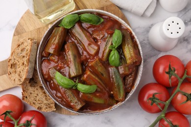 Photo of Tasty stew with okra, tomato sauce and basil on white marble table, flat lay