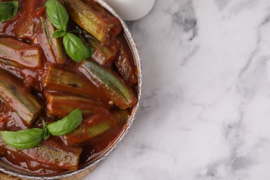 Photo of Tasty stew with okra, tomato sauce and basil on white marble table, top view. Space for text