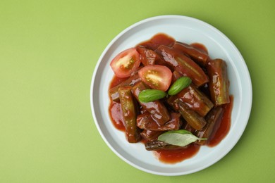 Tasty stew with okra, tomato sauce and basil on light green background, top view. Space for text