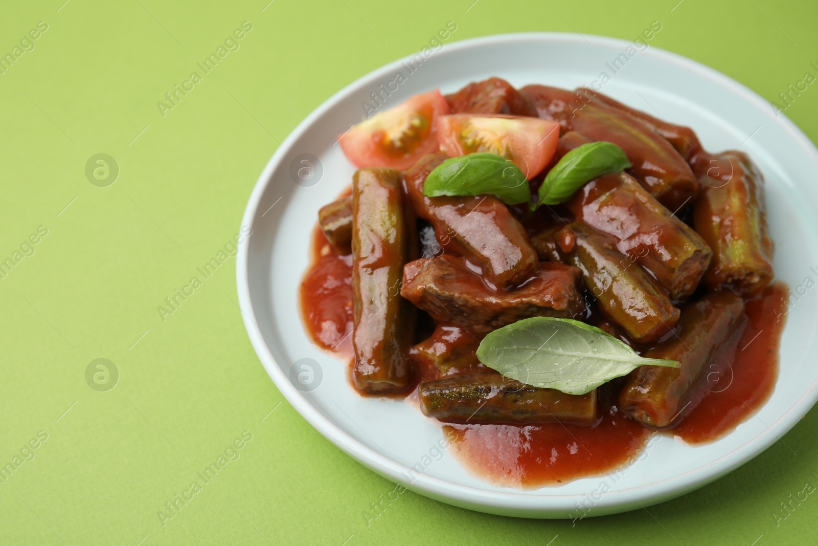 Photo of Tasty stew with okra, tomato sauce and basil on light green background, closeup. Space for text