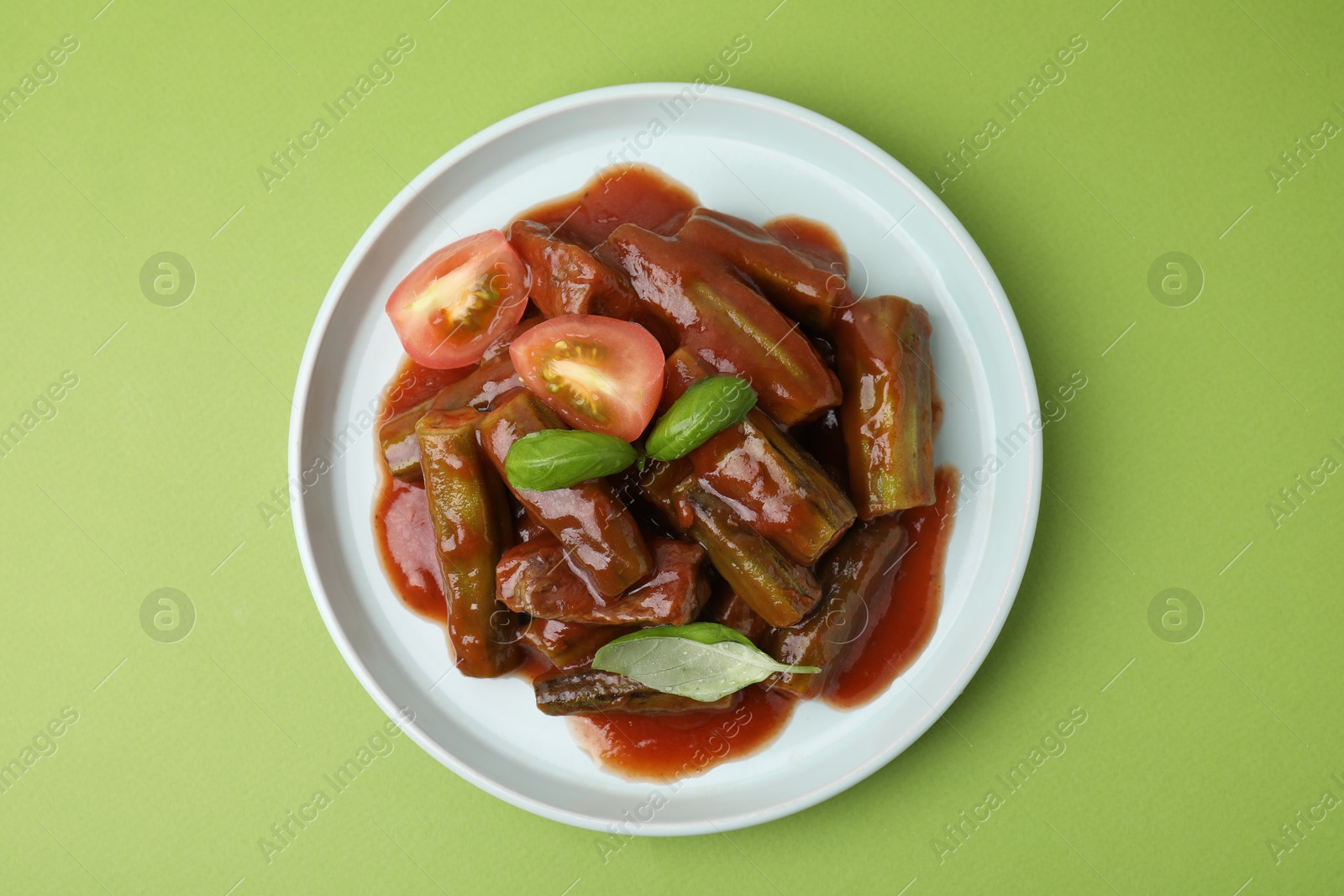 Photo of Tasty stew with okra, tomato sauce and basil on light green background, top view