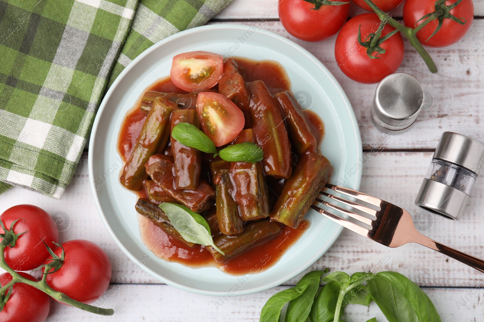 Photo of Tasty stew with okra, tomato sauce and basil on white wooden table, flat lay