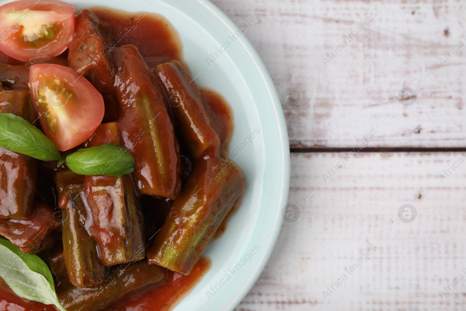 Photo of Tasty stew with okra, tomato sauce and basil on white wooden table, top view. Space for text