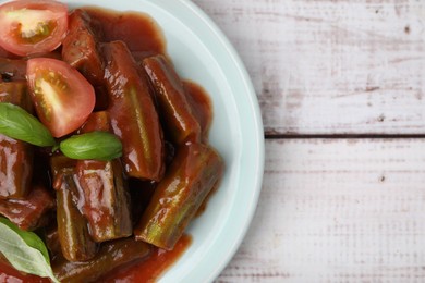 Photo of Tasty stew with okra, tomato sauce and basil on white wooden table, top view. Space for text