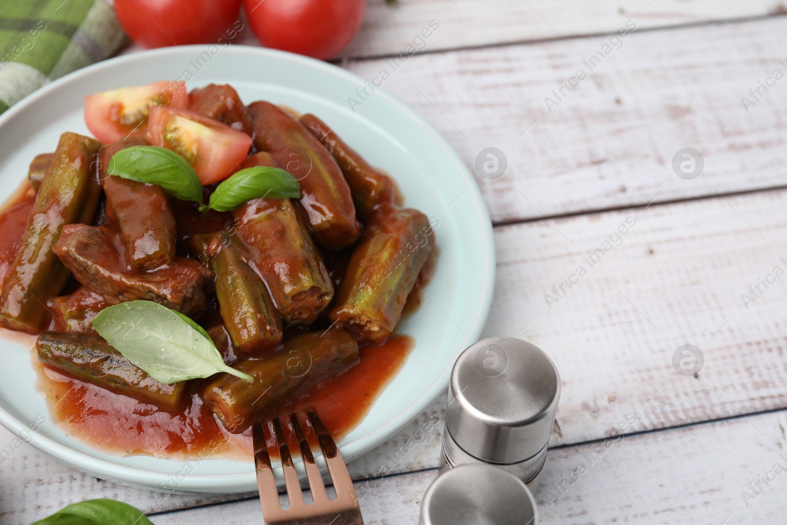 Photo of Tasty stew with okra, tomato sauce and basil on white wooden table, closeup. Space for text