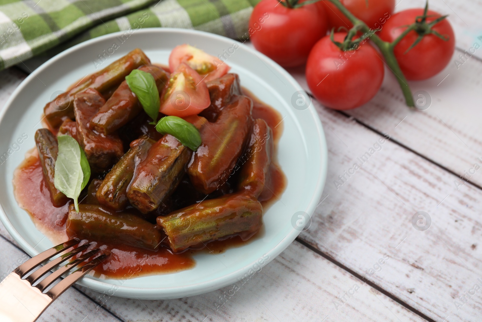 Photo of Tasty stew with okra, tomato sauce and basil on white wooden table, closeup. Space for text