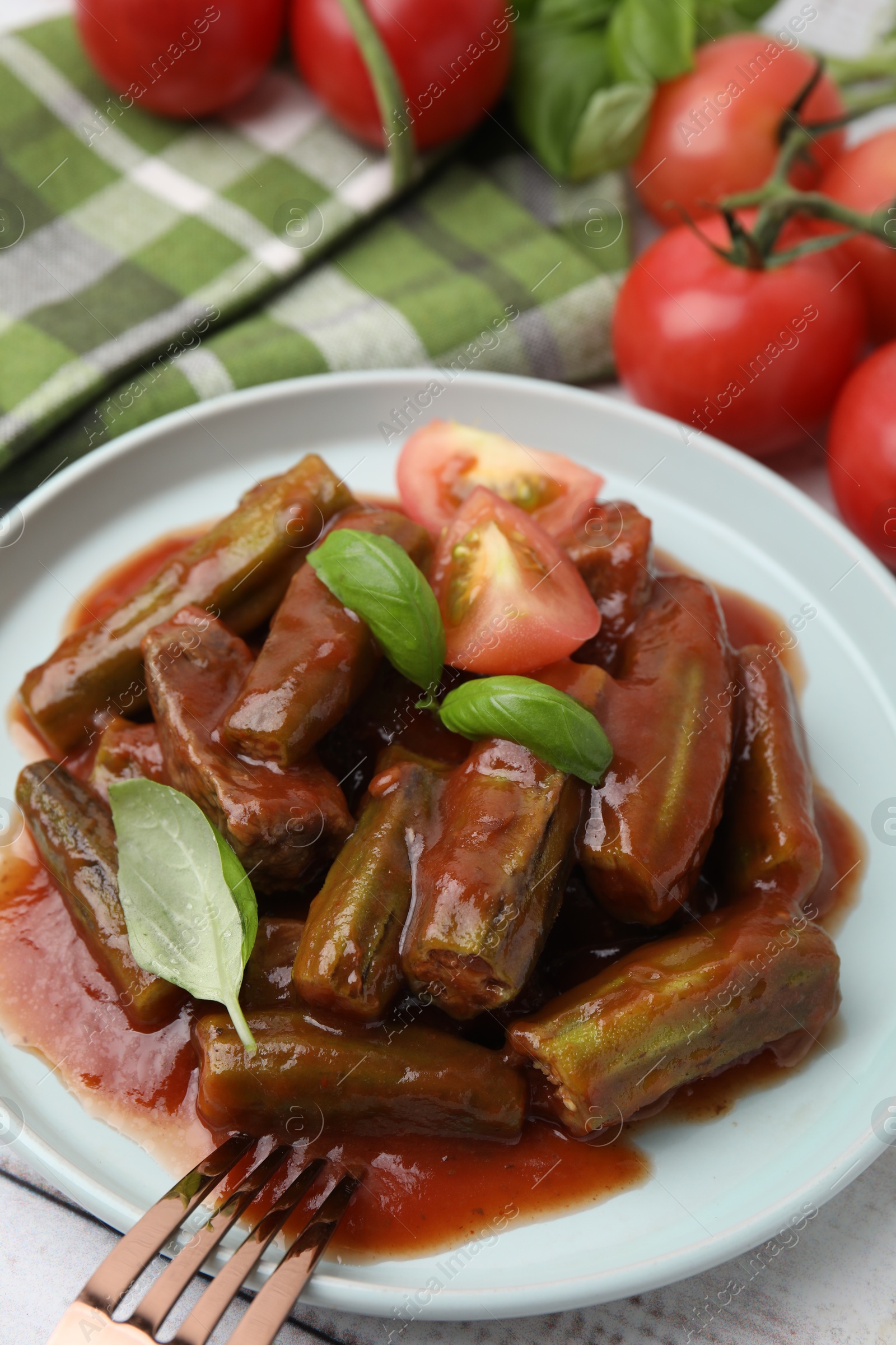 Photo of Tasty stew with okra, tomato sauce and basil on white wooden table, closeup