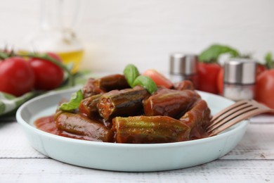 Tasty stew with okra, tomato sauce and basil on white wooden table, closeup