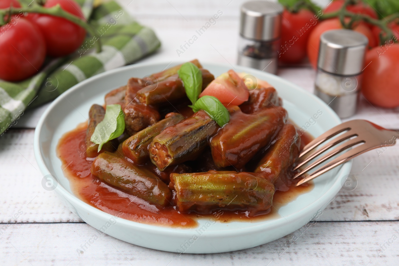 Photo of Tasty stew with okra, tomato sauce and basil on white wooden table, closeup