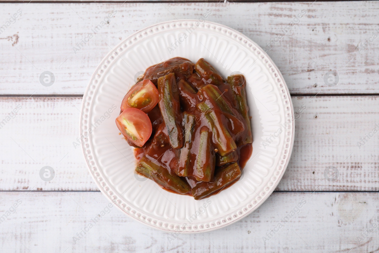 Photo of Tasty stew with okra and tomato sauce on white wooden table, top view