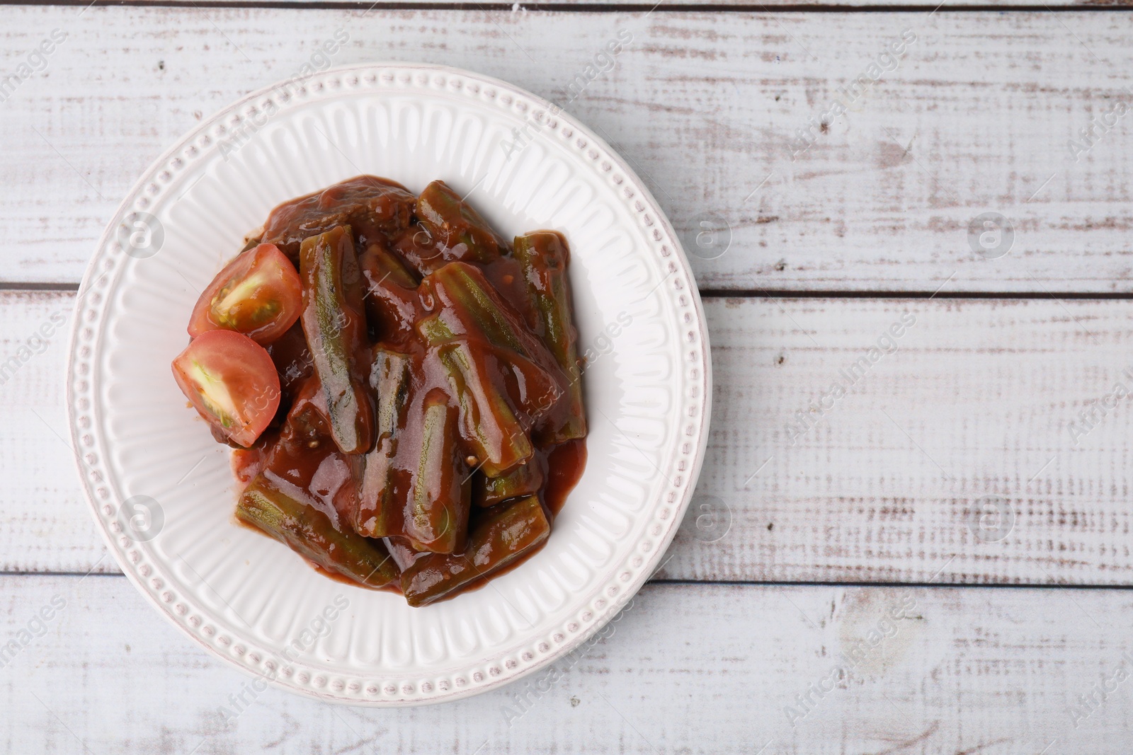 Photo of Tasty stew with okra and tomato sauce on white wooden table, top view. Space for text