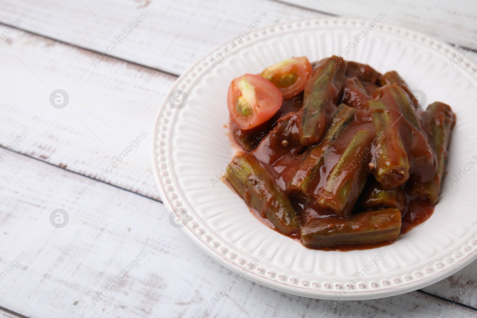 Photo of Tasty stew with okra and tomato sauce on white wooden table, space for text