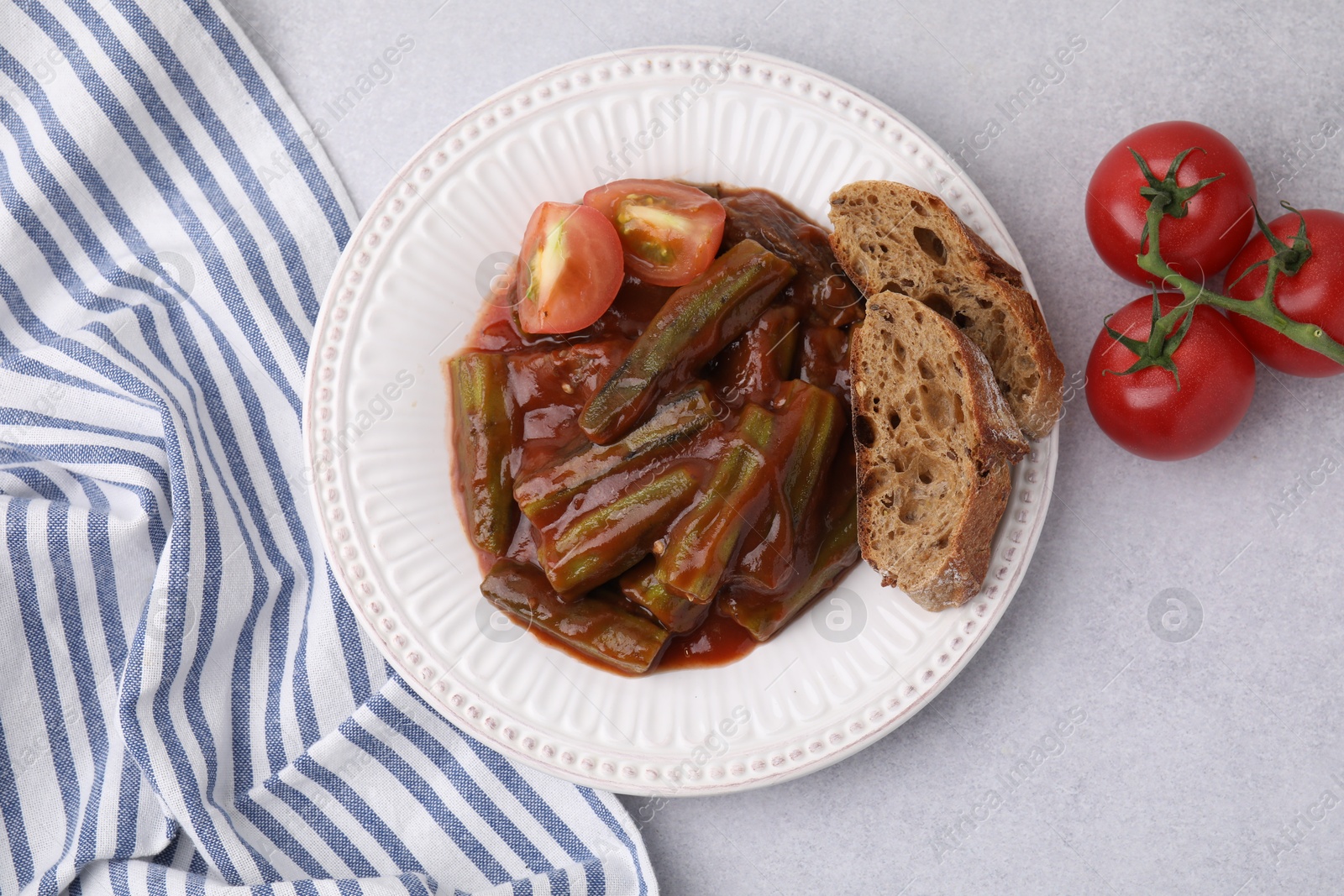 Photo of Tasty stew with okra, tomato sauce and bread on white table, flat lay