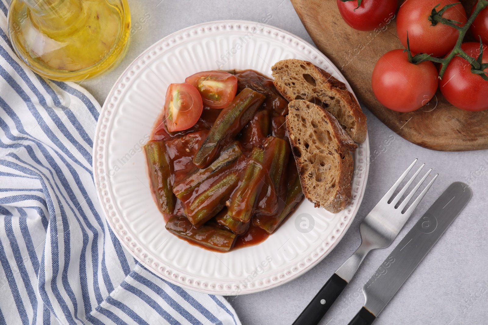 Photo of Tasty stew with okra, tomato sauce and bread on white table, flat lay