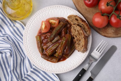 Photo of Tasty stew with okra, tomato sauce and bread on white table, flat lay