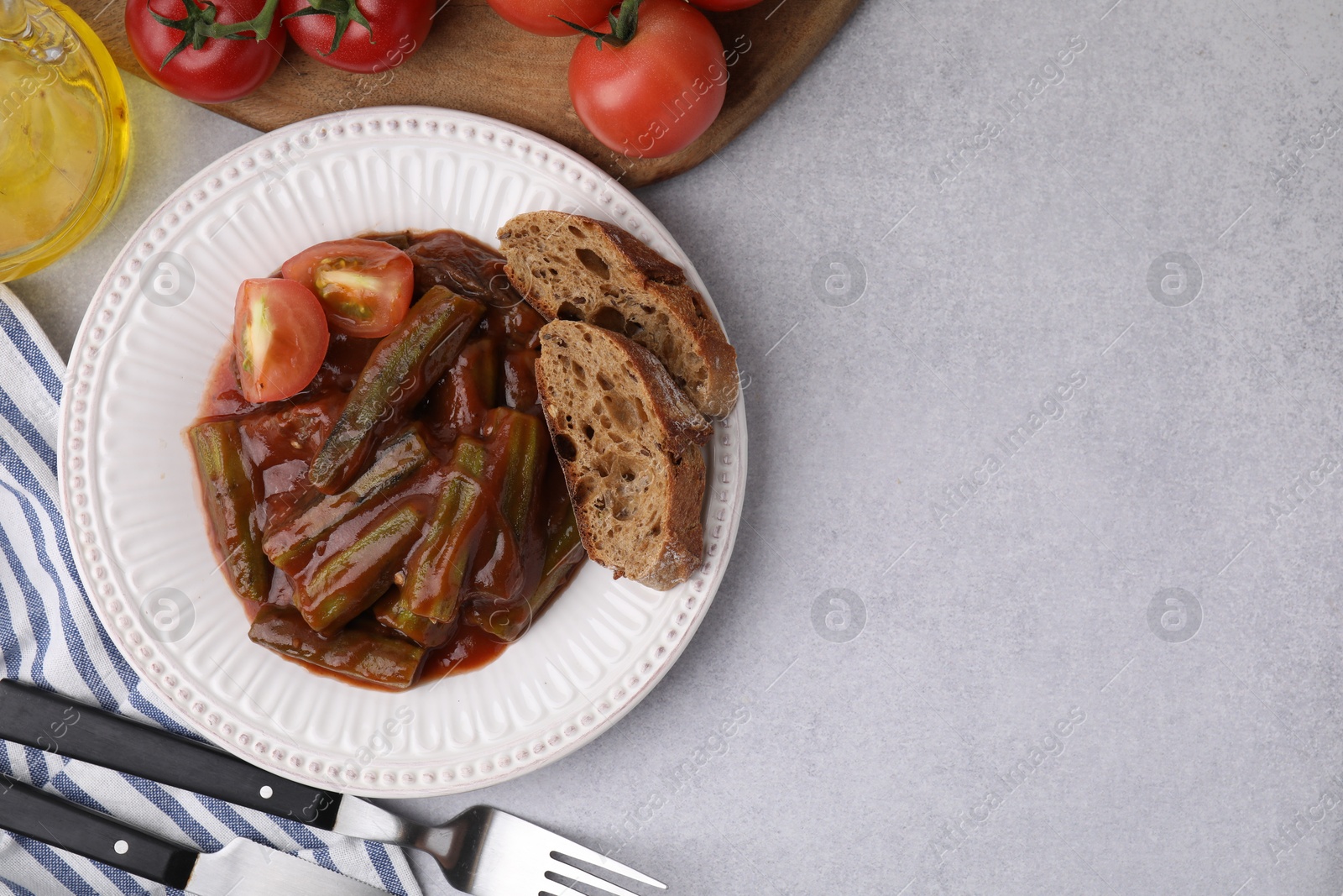 Photo of Tasty stew with okra, tomato sauce and bread on white table, flat lay. Space for text