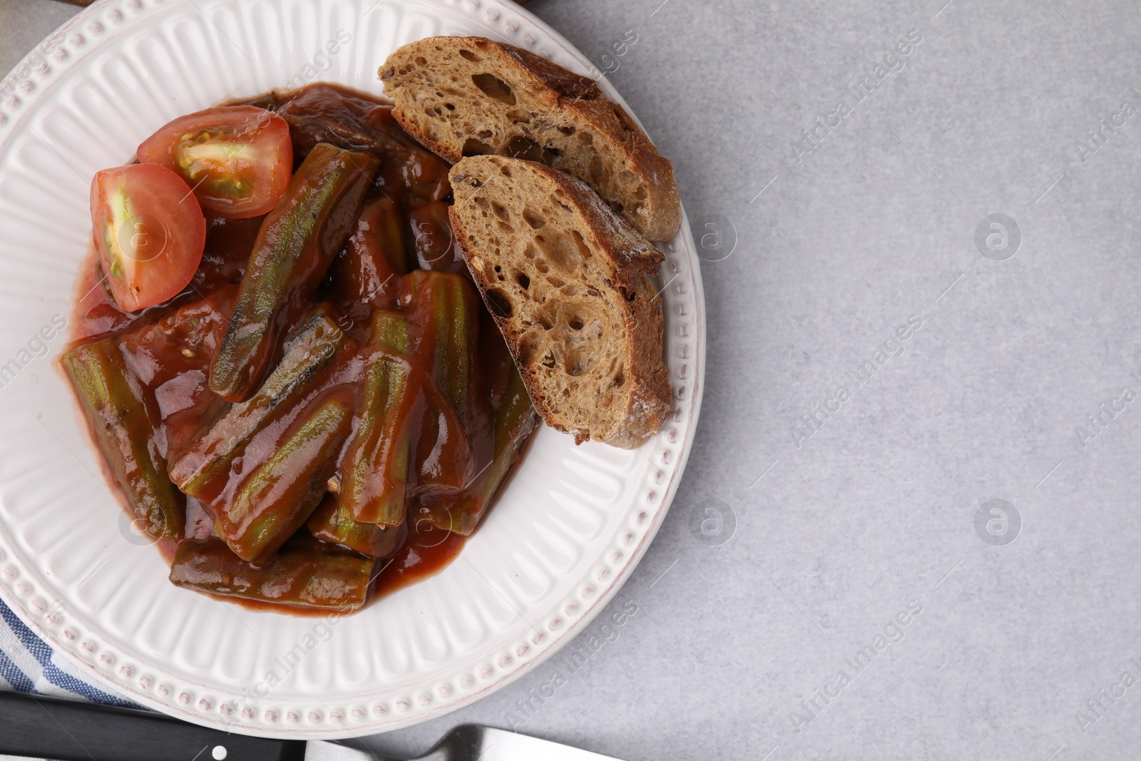 Photo of Tasty stew with okra, tomato sauce and bread on white table, top view. Space for text