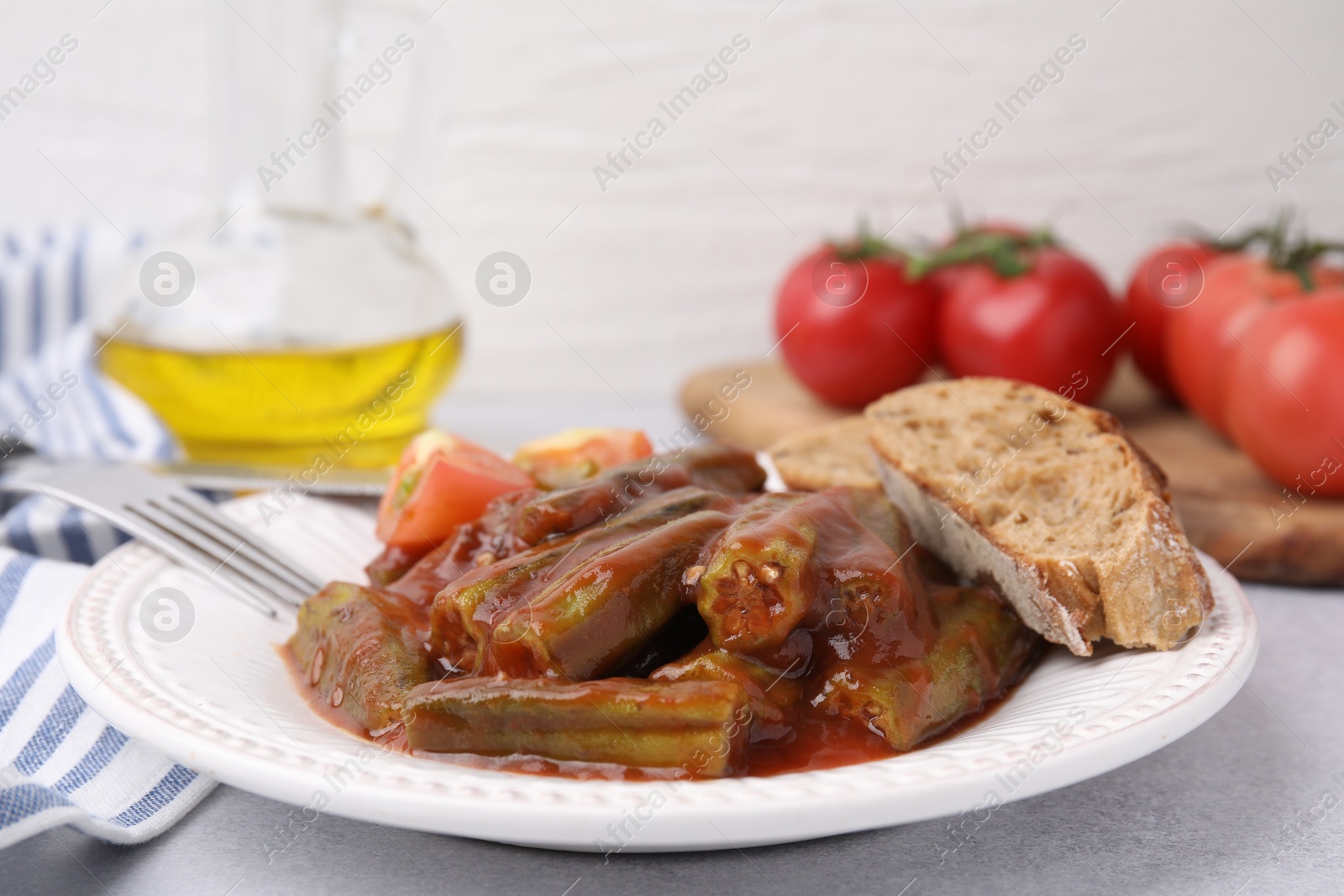 Photo of Tasty stew with okra, tomato sauce and bread on white table, closeup