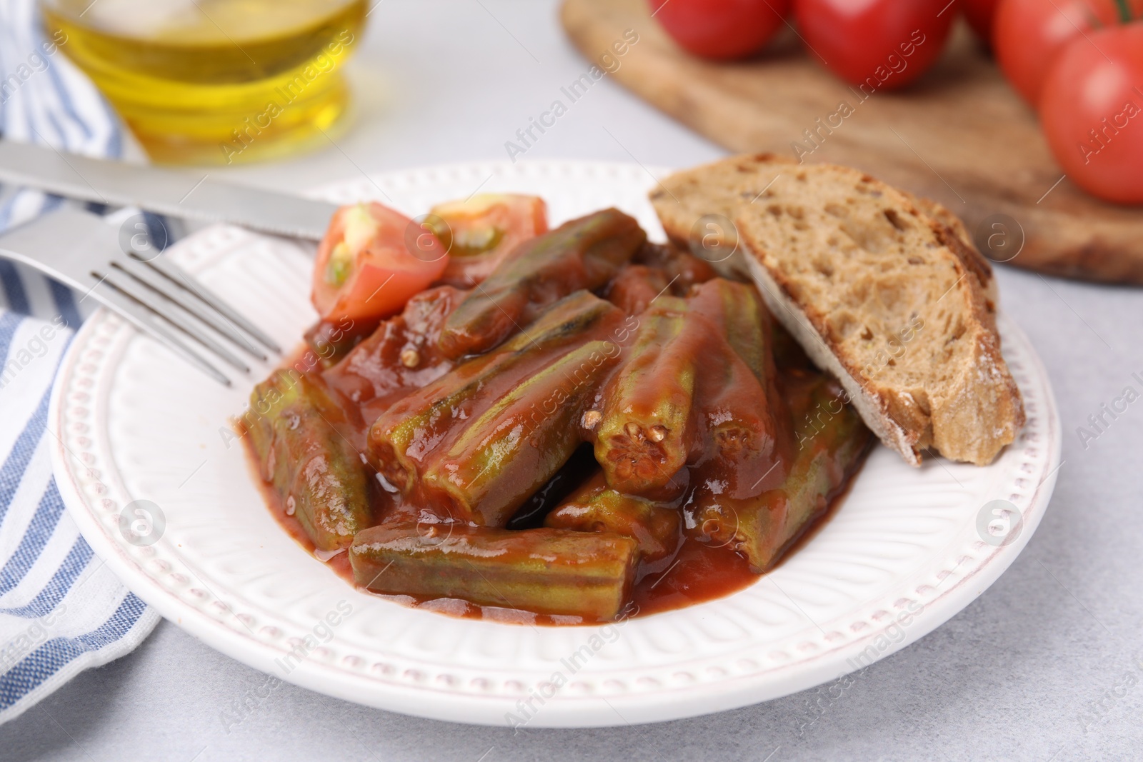 Photo of Tasty stew with okra, tomato sauce and bread on white table, closeup