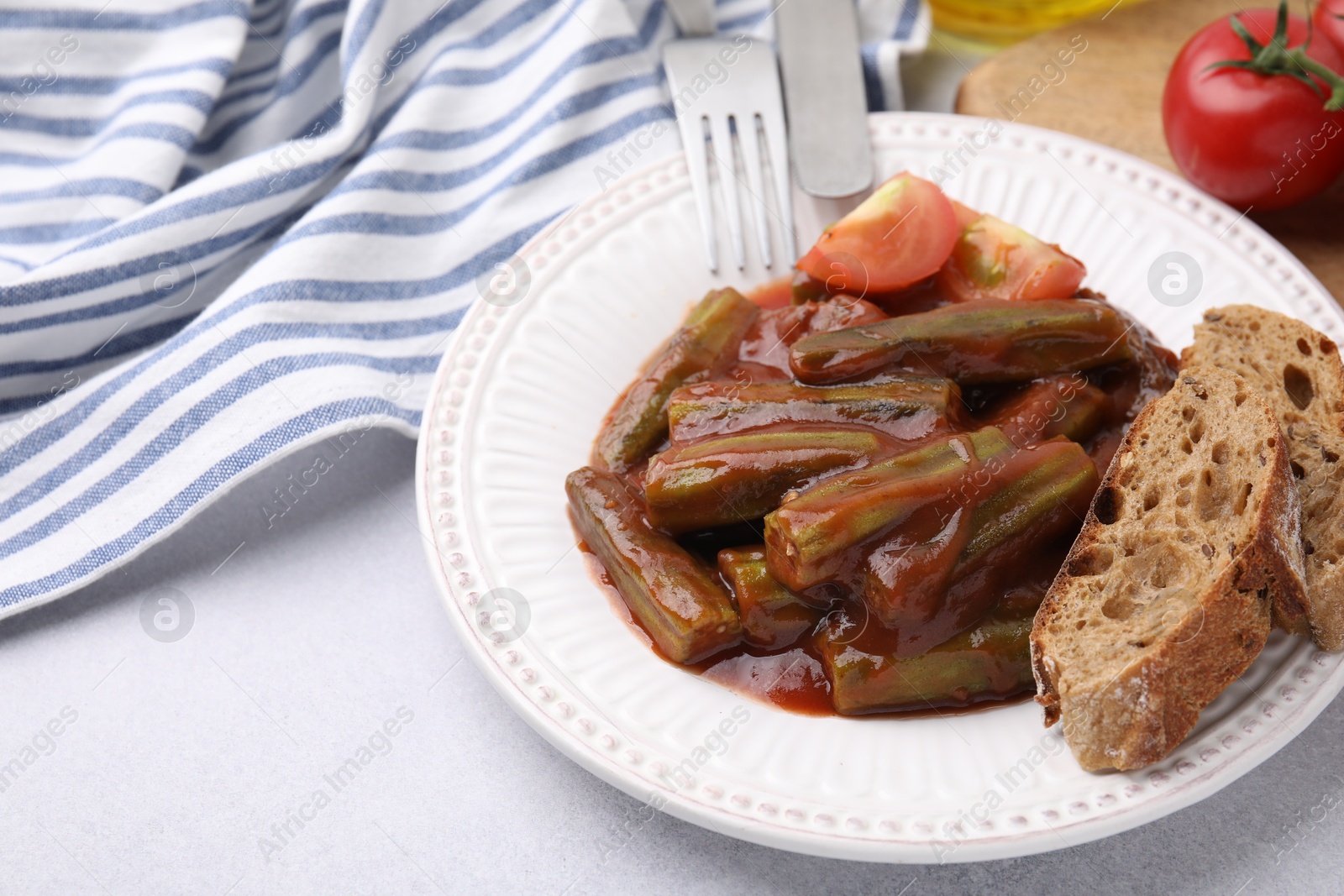 Photo of Tasty stew with okra, tomato sauce and bread on white table, closeup. Space for text