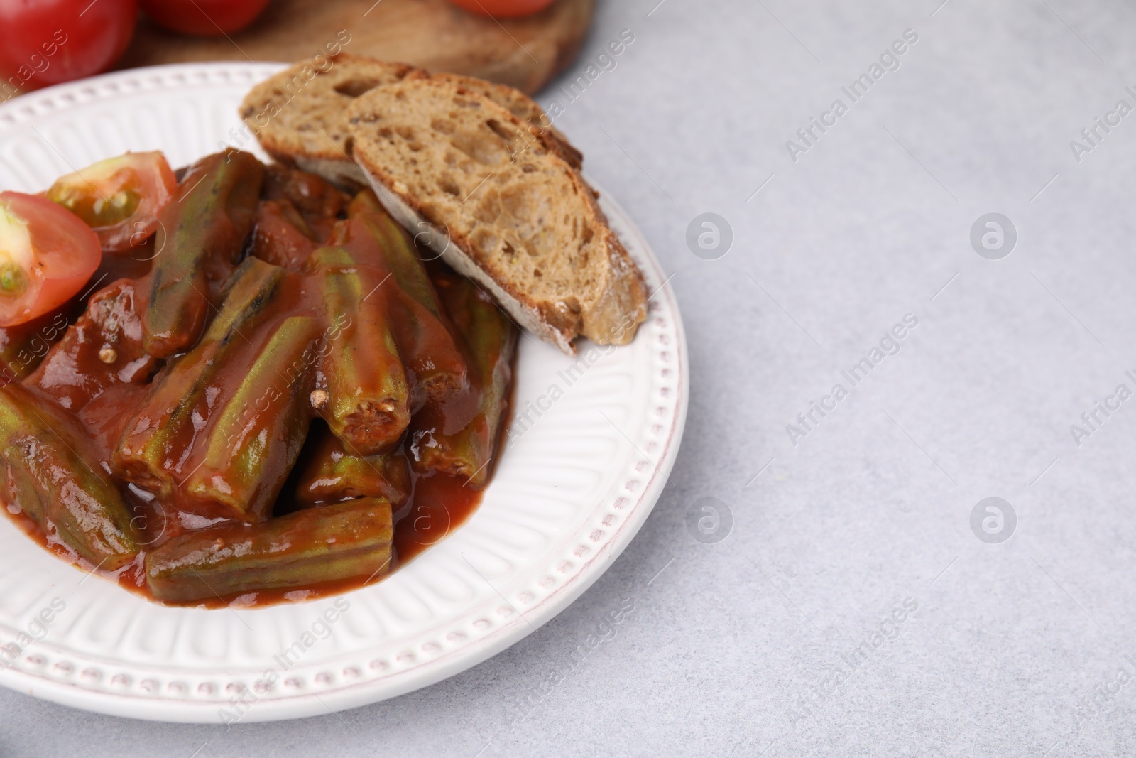 Photo of Tasty stew with okra, tomato sauce and bread on white table, closeup. Space for text