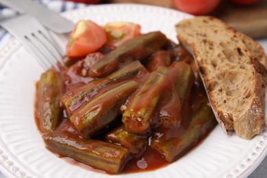 Photo of Tasty stew with okra, tomato sauce and bread on table, closeup