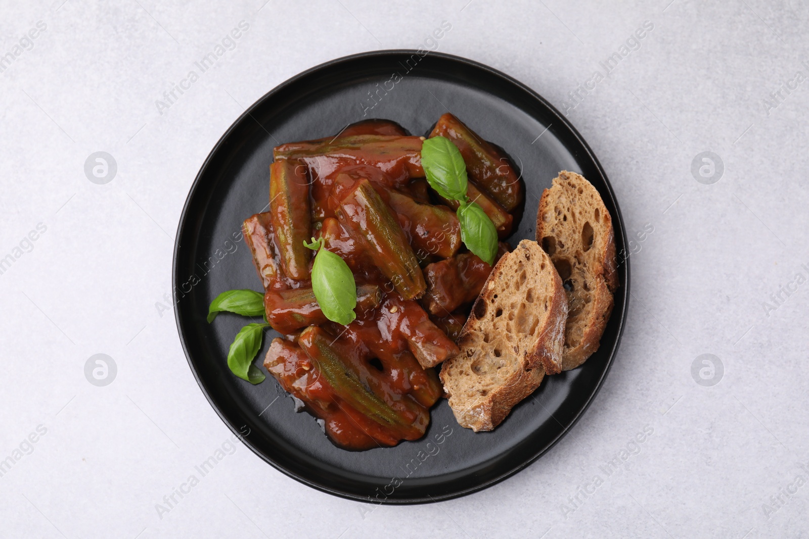 Photo of Tasty stew with okra, tomato sauce, bread and basil on white table, top view