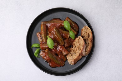 Tasty stew with okra, tomato sauce, bread and basil on white table, top view