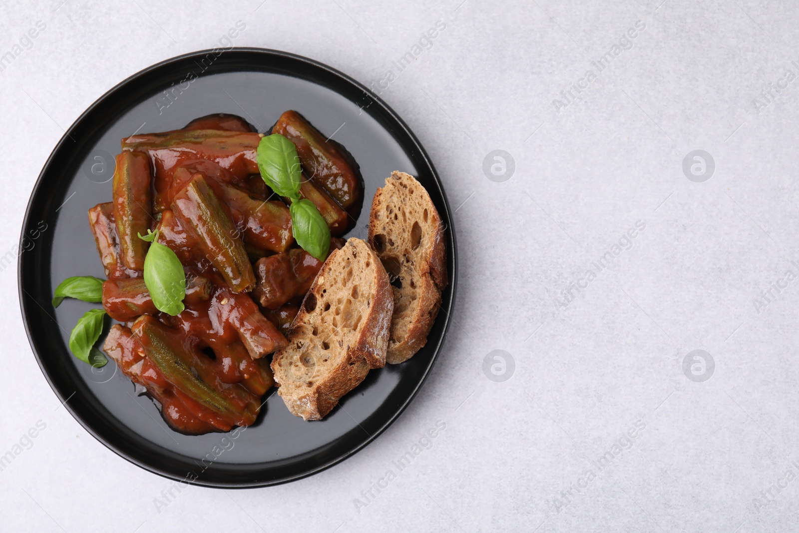 Photo of Tasty stew with okra, tomato sauce, bread and basil on white table, top view. Space for text