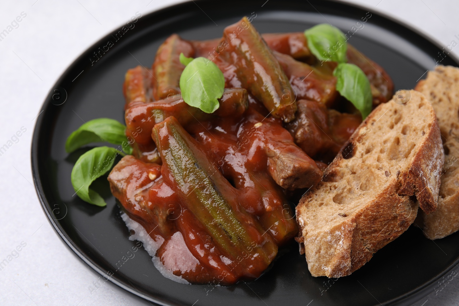 Photo of Tasty stew with okra, tomato sauce, bread and basil on white table, closeup