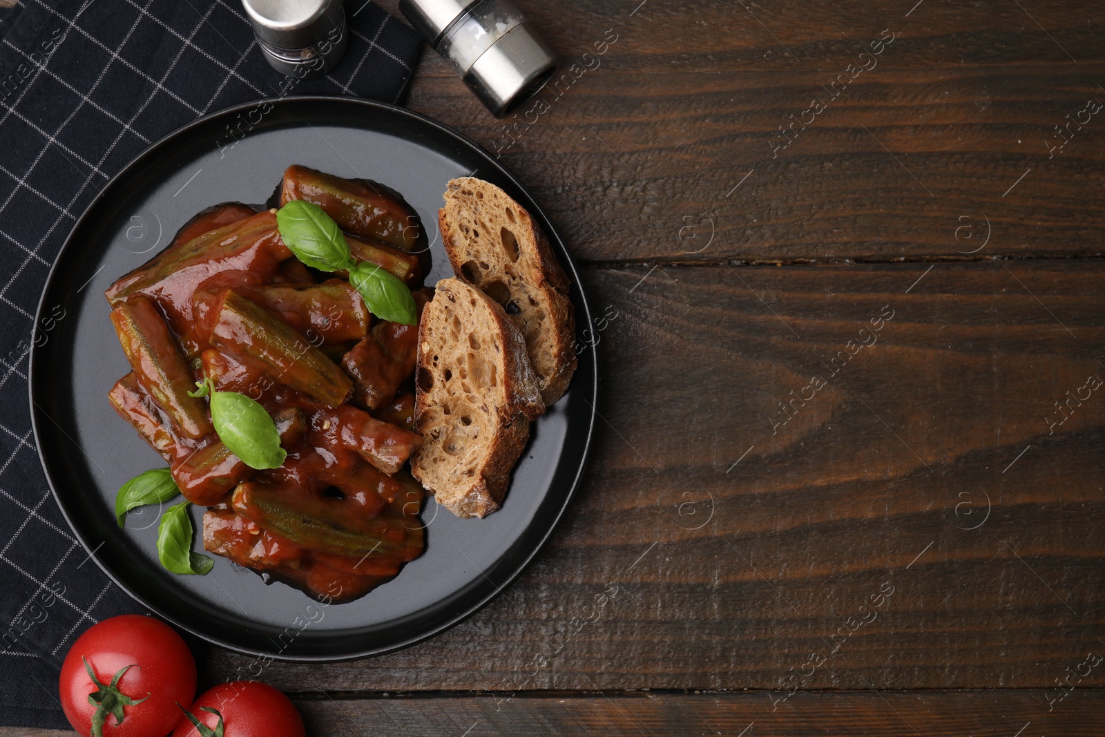 Photo of Tasty stew with okra, tomato sauce, bread and basil on wooden table, flat lay. Space for text