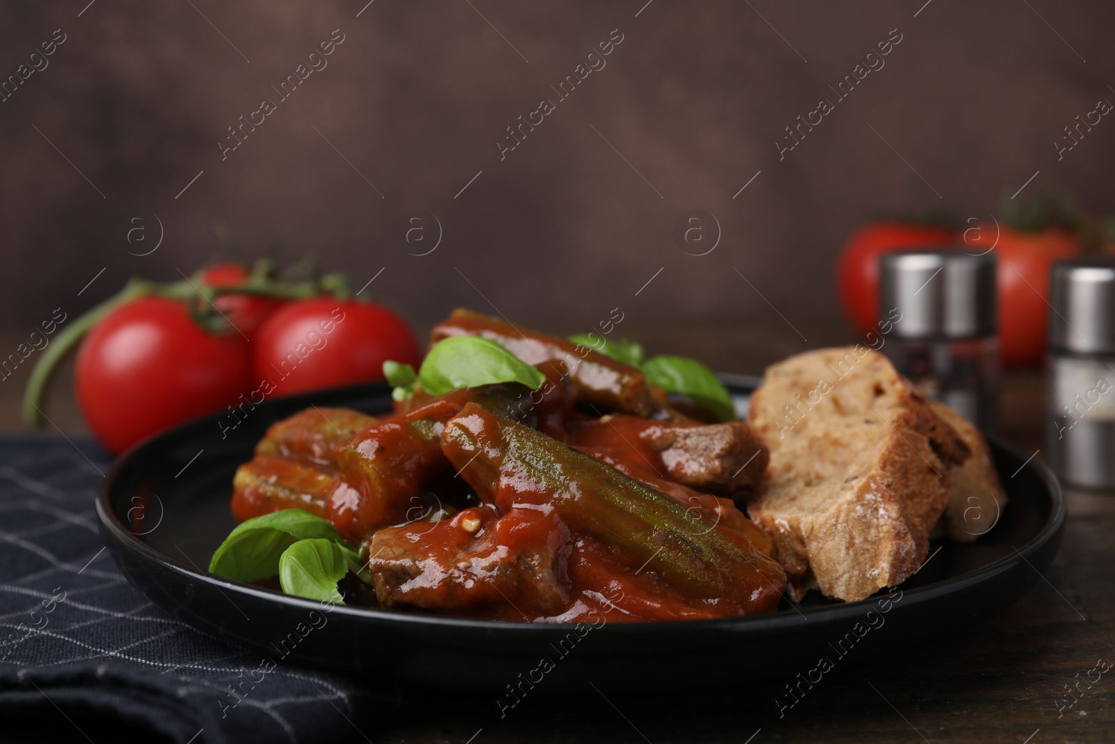 Photo of Tasty stew with okra, tomato sauce, bread and basil on wooden table, closeup