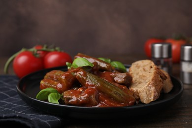 Photo of Tasty stew with okra, tomato sauce, bread and basil on wooden table, closeup