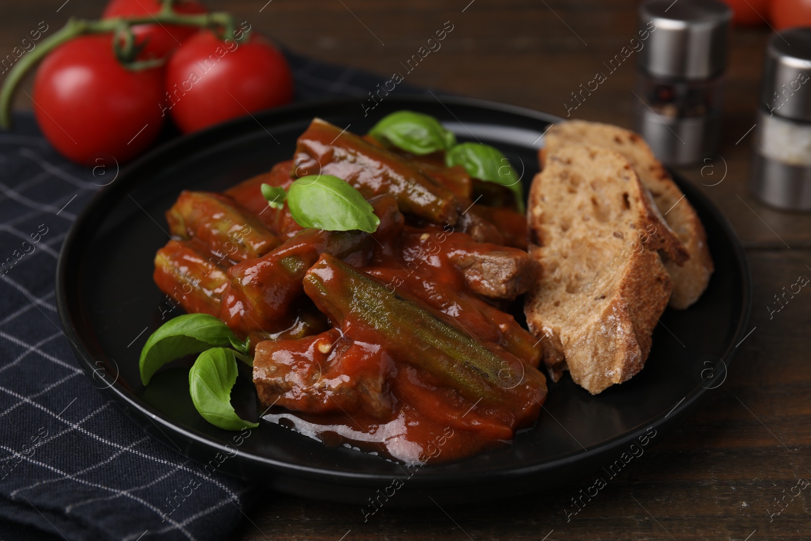 Photo of Tasty stew with okra, tomato sauce, bread and basil on wooden table, closeup